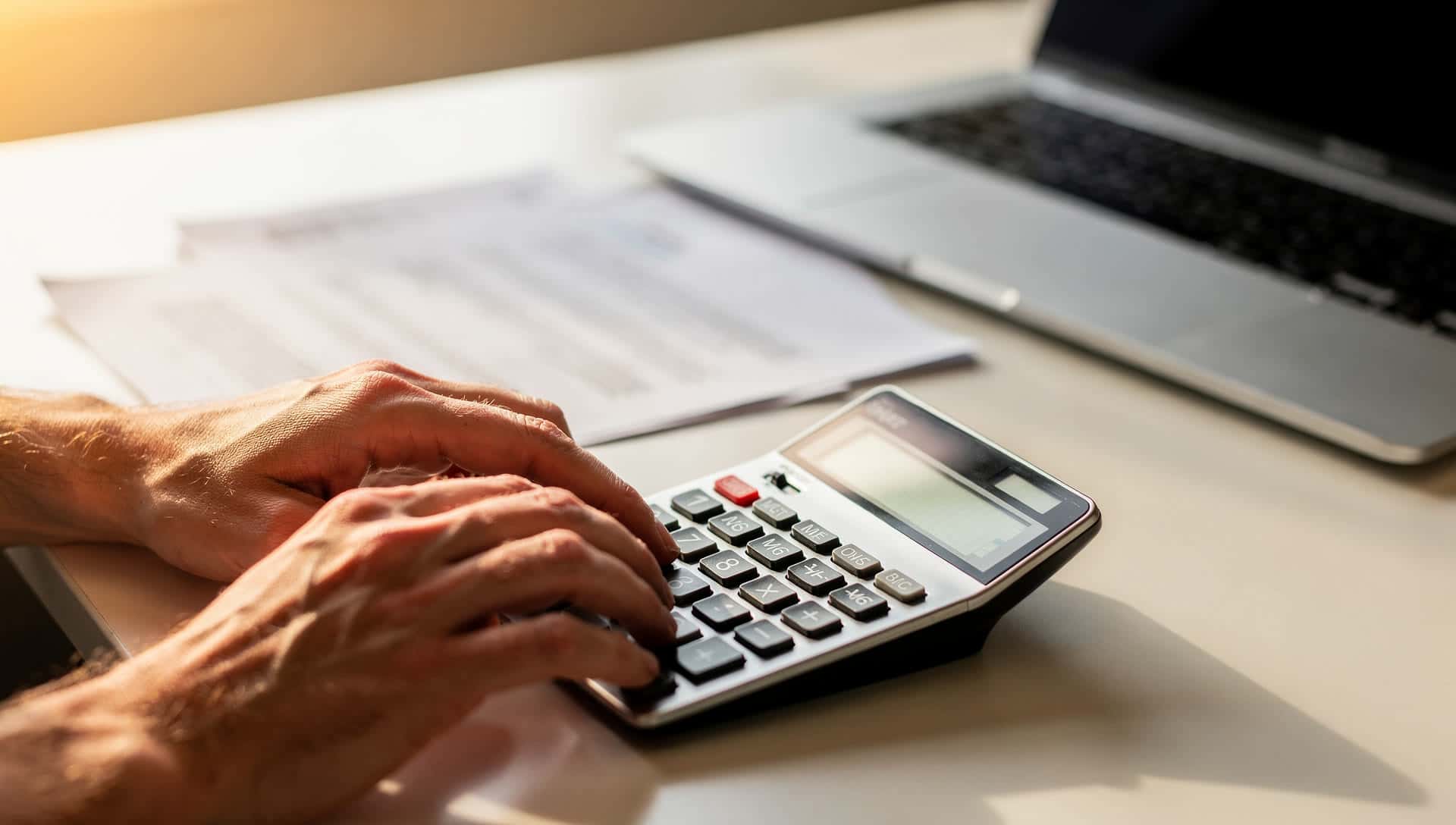A hand using a calculator beside a processing statement on a modern desk