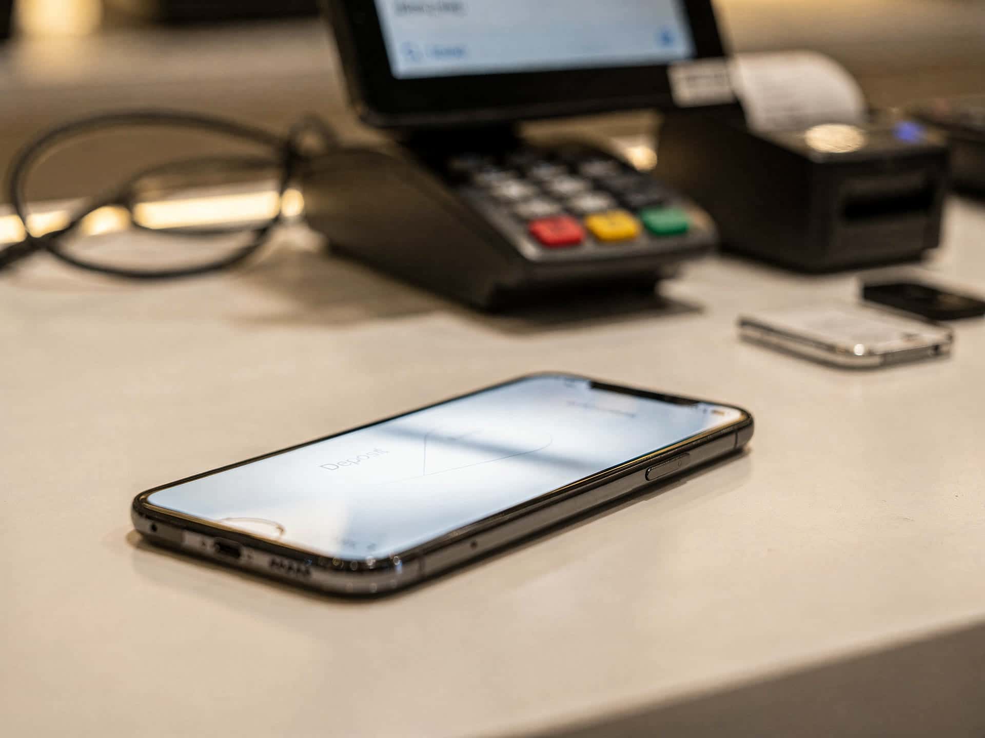 A phone showing a same-day bank deposit notification next to a store register